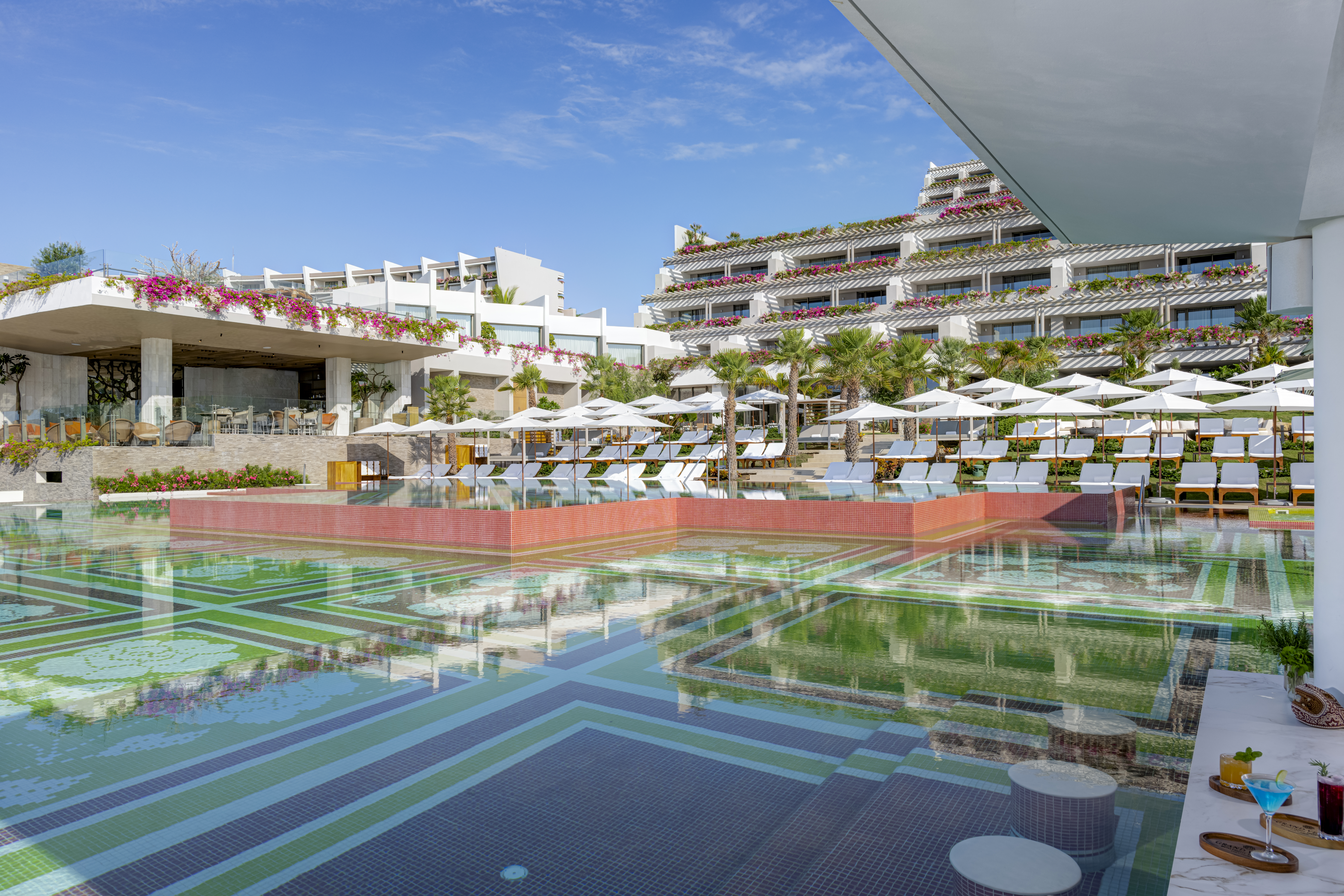 Infinity pool with colorful mosaic tiles and loungers overlooking the ocean