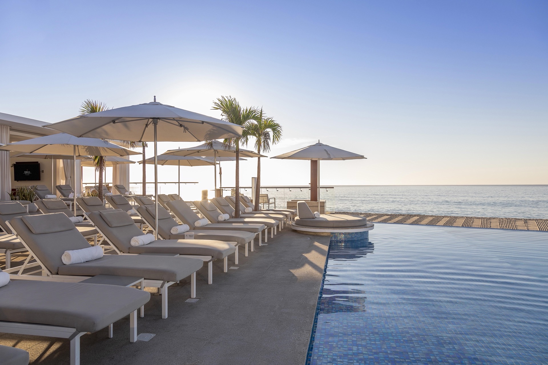 Beachfront infinity pool with plush loungers and ocean views at sunset