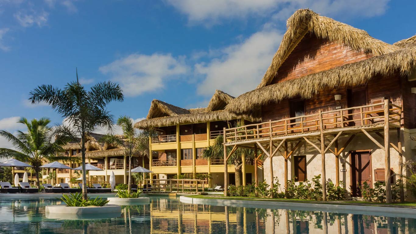 Palapa-roofed suite buildings reflected in the serpentine infinity pool at golden hour