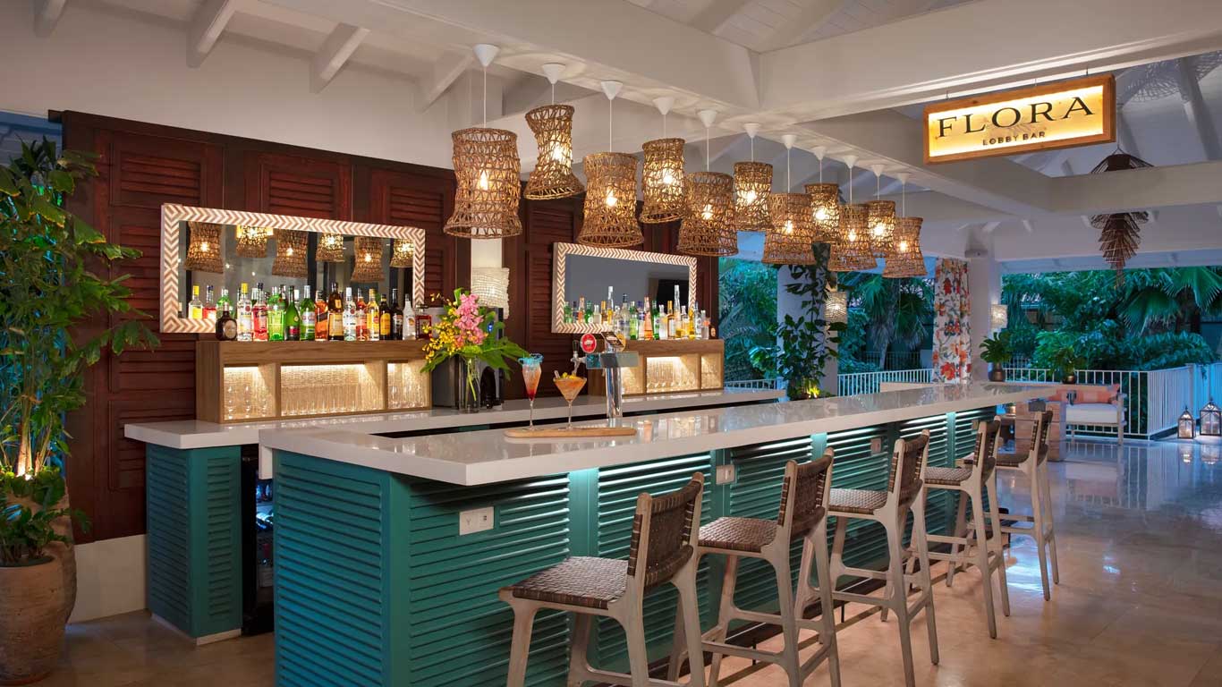 Flora Lobby Bar with teal louvered bar front, woven rattan pendant lights, and premium spirits display