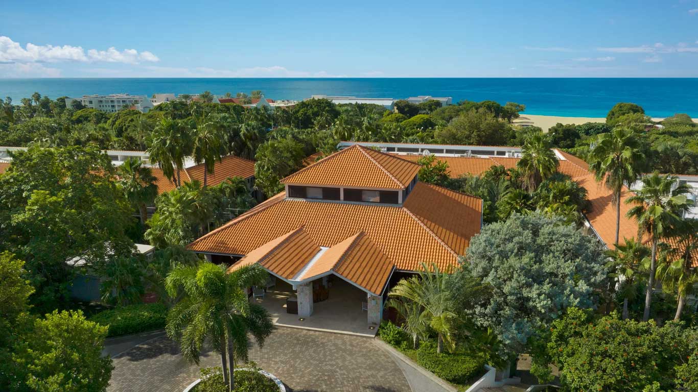 Aerial view of the resort entrance and terracotta-roofed buildings surrounded by palms with Caribbean Sea in background
