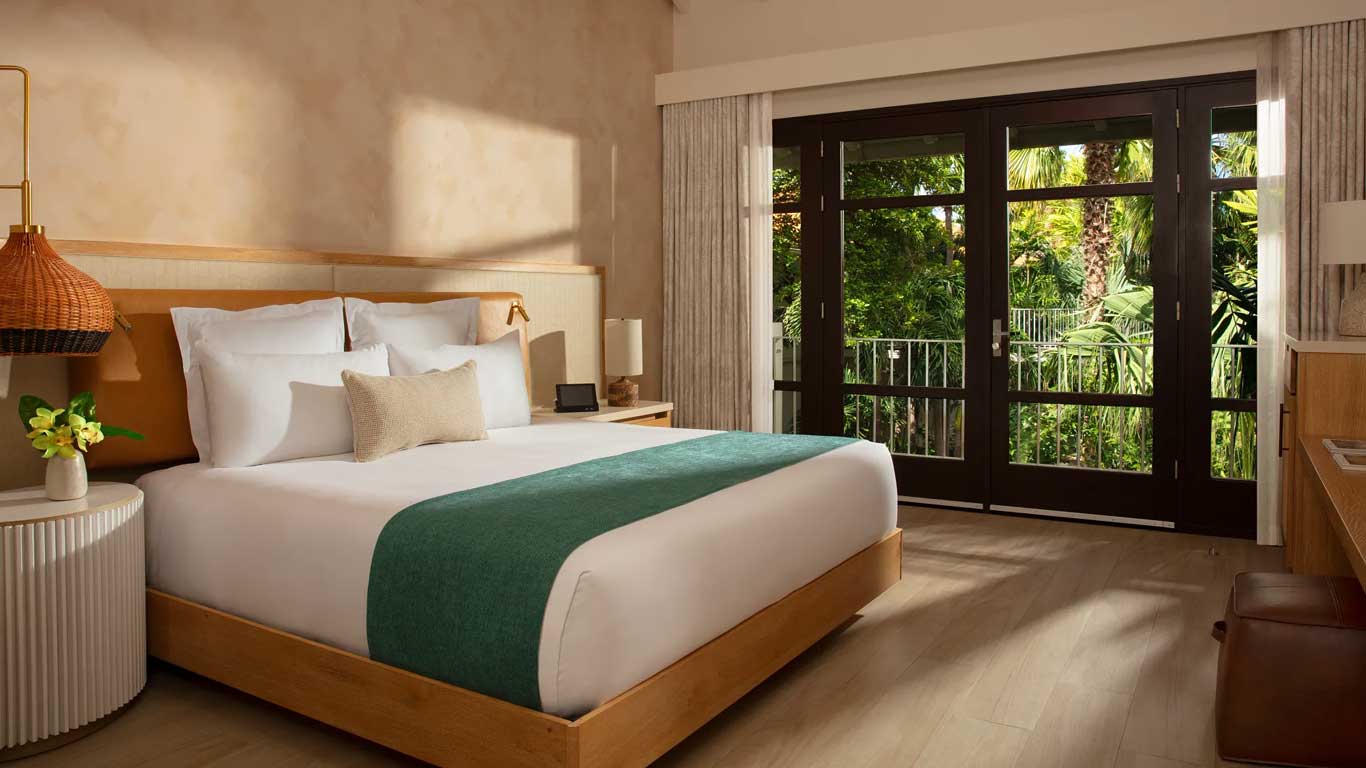 Junior Suite bedroom with king bed, teal runner, natural wood furniture, and tropical garden balcony view