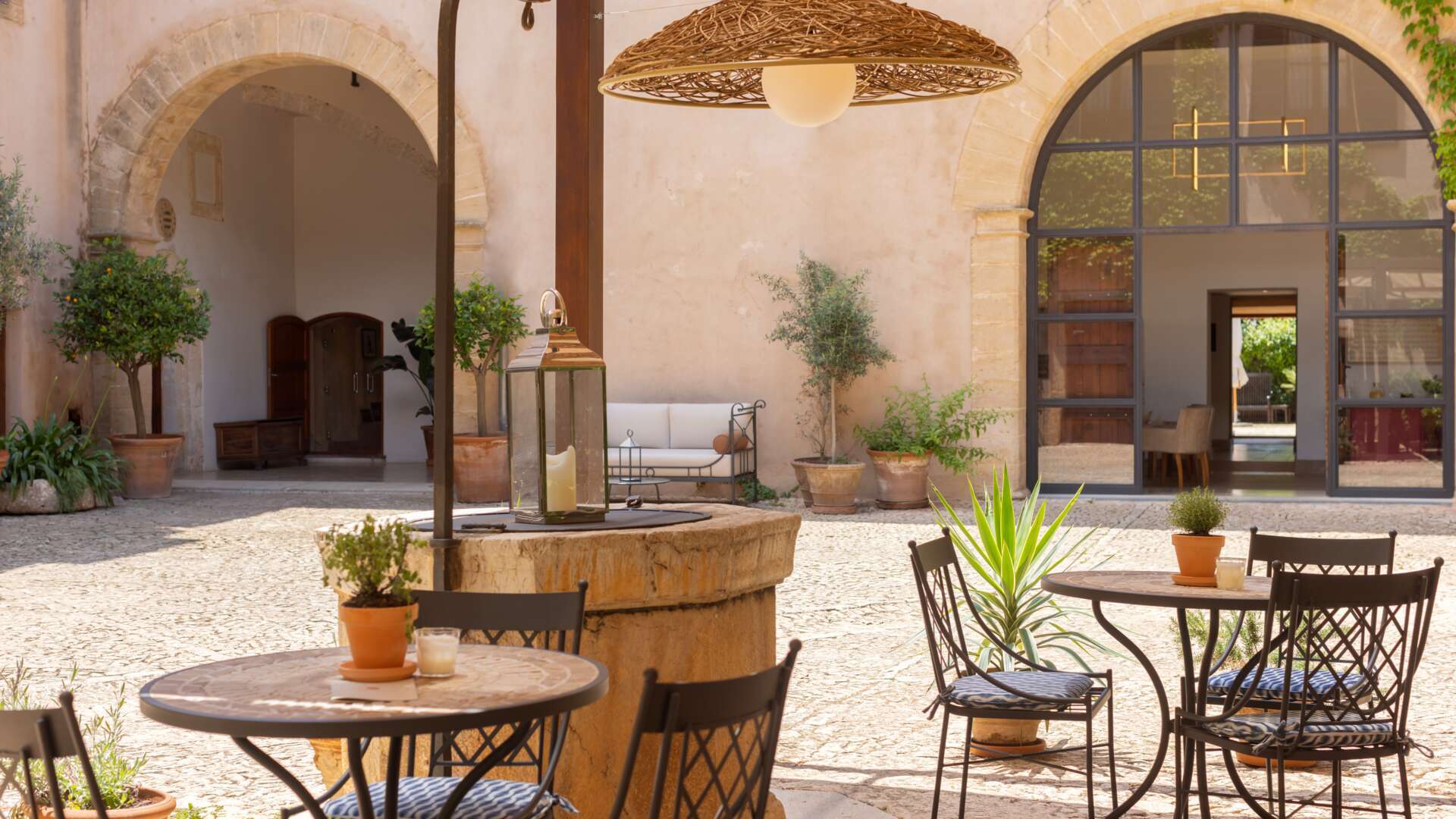 Intimate courtyard dining detail with centuries-old stone well, wrought-iron bistro tables, and traditional Mallorcan architecture