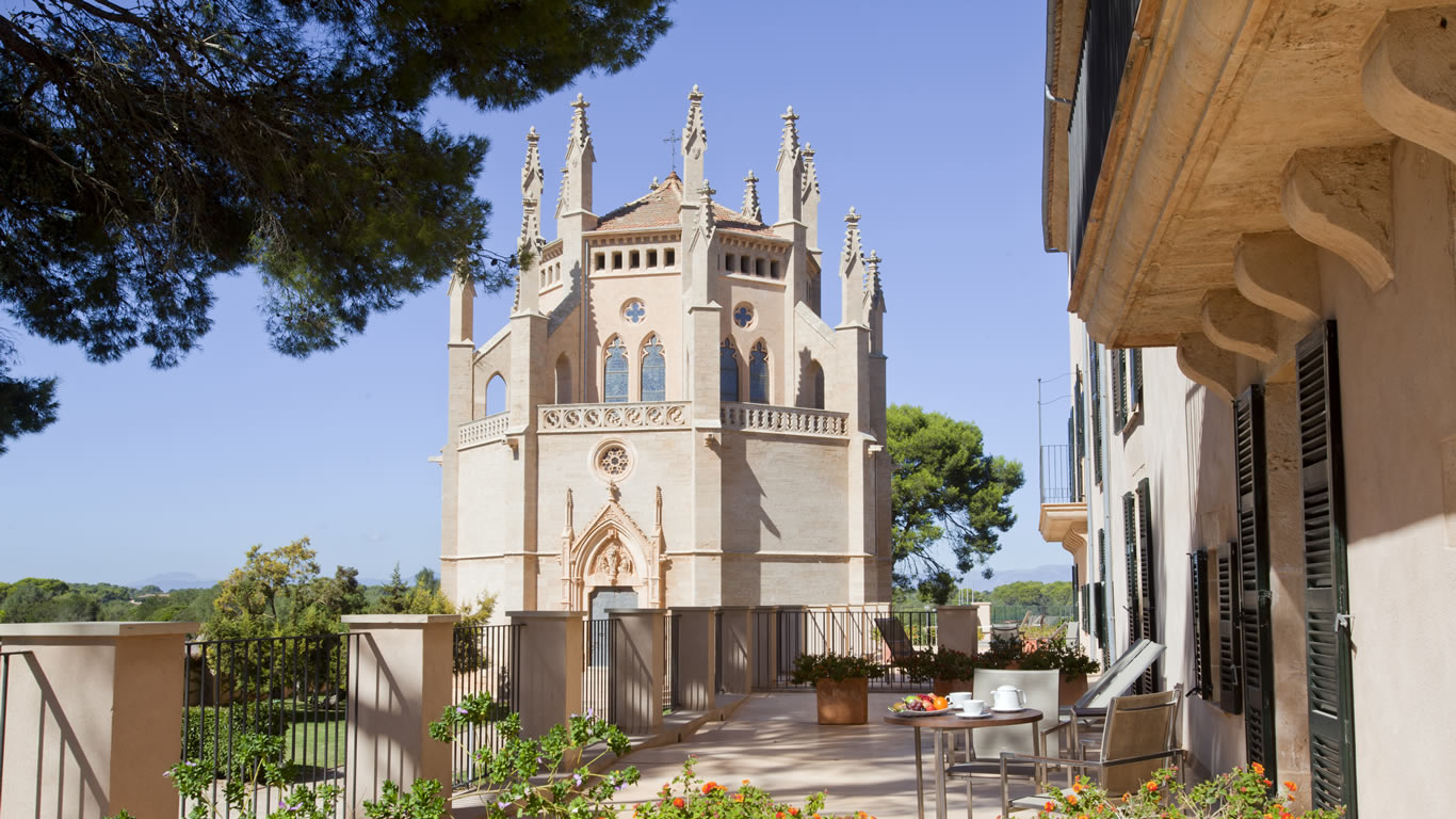 Neo-Gothic chapel La Gran Cristiana viewed from a manor house terrace with breakfast setting and Mediterranean pines