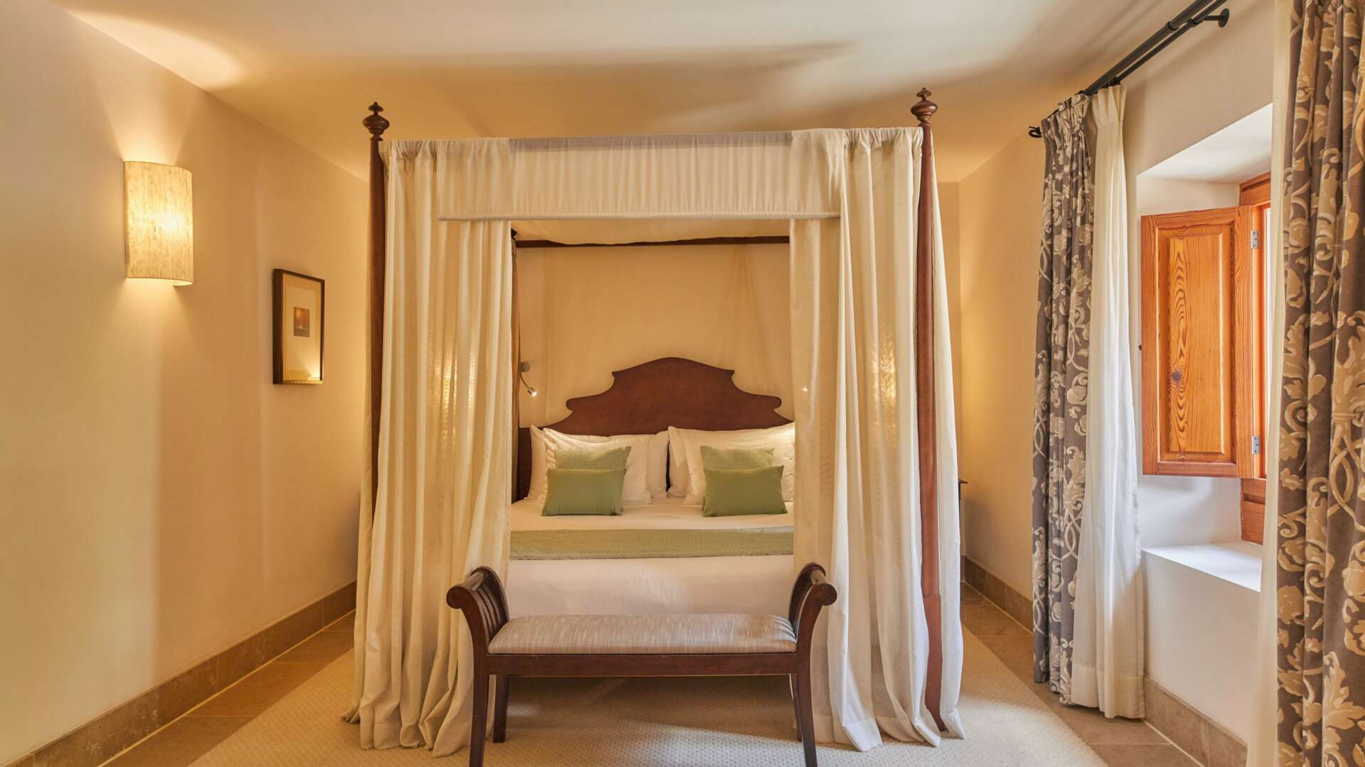 Double Tramuntana Room with classic four-poster canopy bed, sage green accents, and warm amber lighting