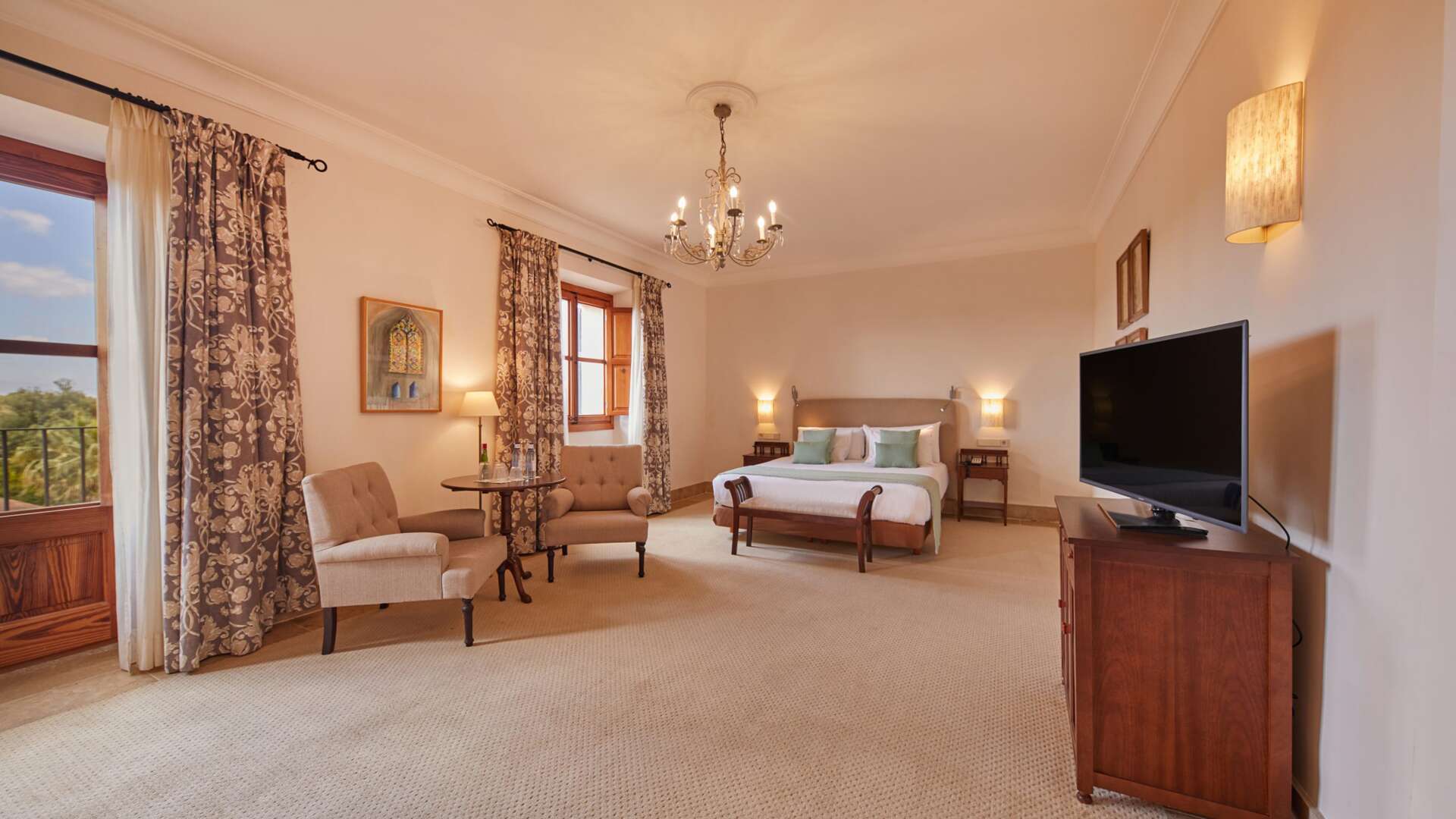 Double Deluxe Tramuntana Room with king bed, wrought-iron chandelier, upholstered sitting area, and countryside views