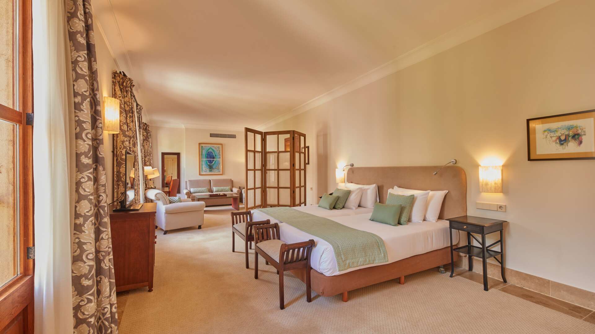 Junior Suite Tramuntana with king bed, wooden folding screen, sage throw, and separate lounge area with sofa